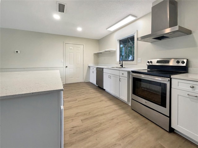 kitchen featuring light wood-type flooring, stainless steel appliances, visible vents, and wall chimney exhaust hood