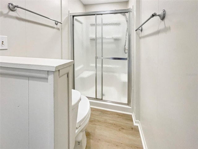 bathroom featuring wood finished floors, toilet, and a stall shower