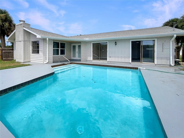 back of property with french doors, board and batten siding, an outdoor pool, a chimney, and a patio area