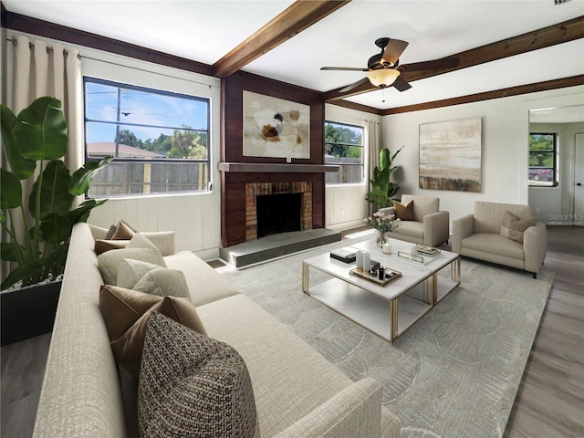 living room featuring ceiling fan, beamed ceiling, a brick fireplace, and wood finished floors