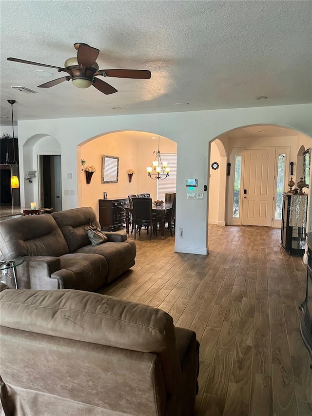 living room with ceiling fan with notable chandelier, wood-type flooring, and a textured ceiling