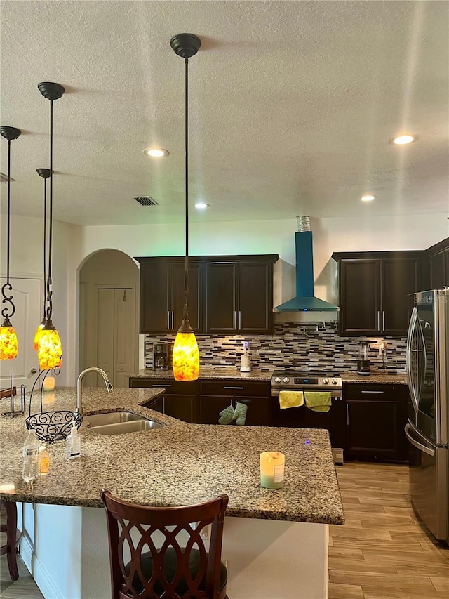 kitchen with light hardwood / wood-style flooring, sink, hanging light fixtures, wall chimney exhaust hood, and appliances with stainless steel finishes