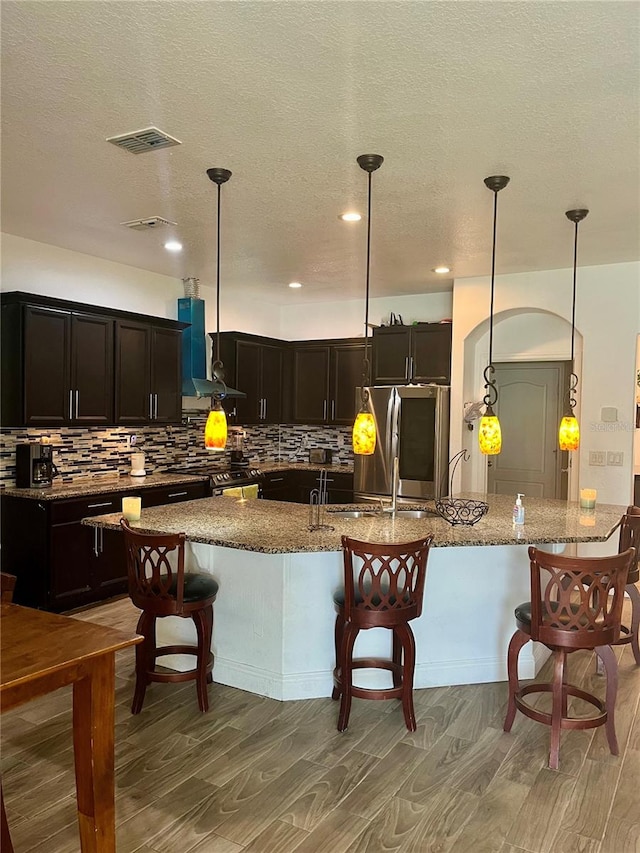 kitchen with hardwood / wood-style floors, appliances with stainless steel finishes, light stone countertops, and extractor fan