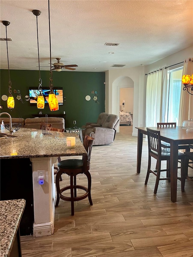 kitchen with light stone countertops, ceiling fan, wood-type flooring, pendant lighting, and a textured ceiling