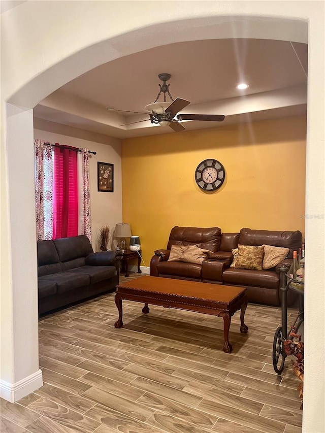 living room featuring a raised ceiling, ceiling fan, and wood-type flooring