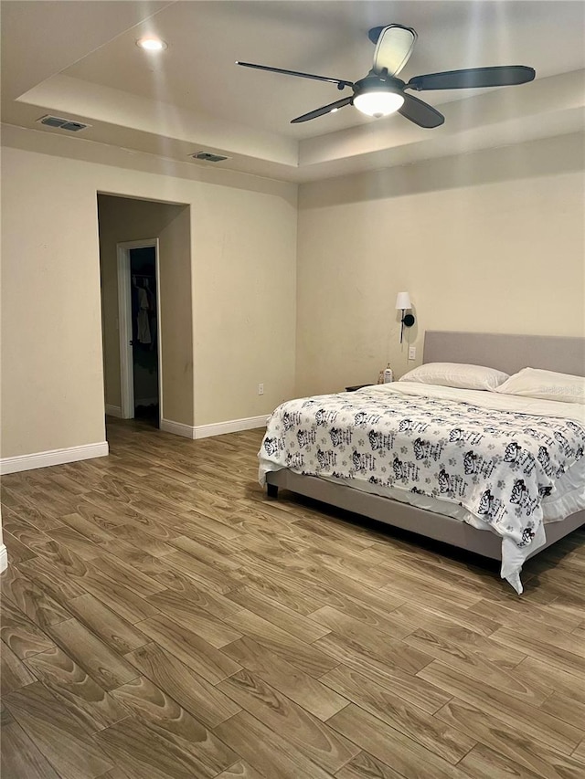 bedroom with ceiling fan, hardwood / wood-style floors, and a tray ceiling