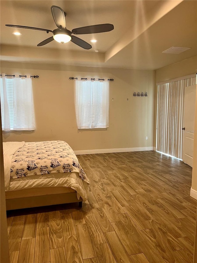 bedroom with multiple windows, ceiling fan, a raised ceiling, and wood-type flooring