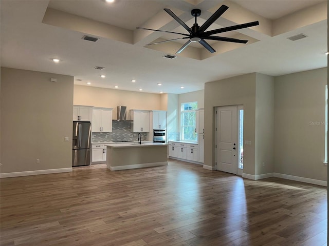 kitchen with wood-type flooring, stainless steel fridge, white cabinetry, an island with sink, and wall chimney exhaust hood