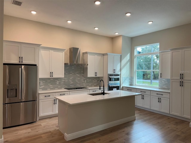 kitchen featuring light wood-type flooring, wall chimney range hood, sink, and stainless steel appliances