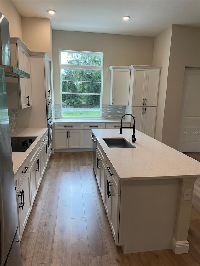 kitchen with stainless steel appliances, white cabinetry, sink, wall chimney range hood, and light wood-type flooring