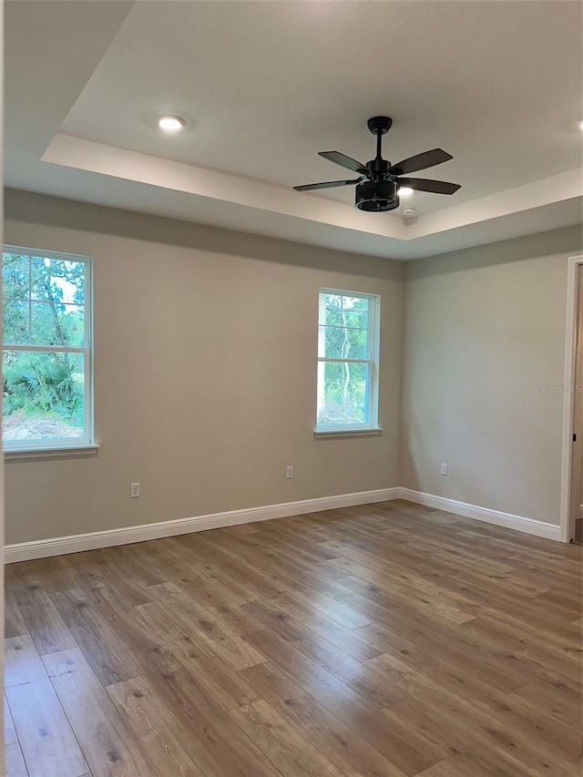 unfurnished room with ceiling fan, wood-type flooring, and a tray ceiling