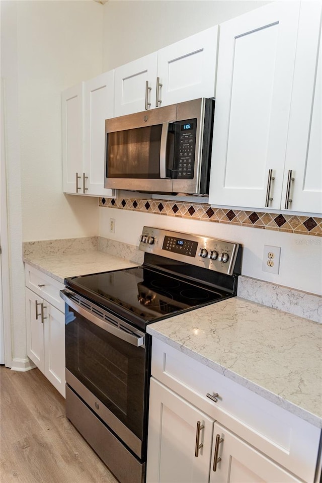 kitchen featuring appliances with stainless steel finishes, light stone counters, white cabinets, and light hardwood / wood-style floors