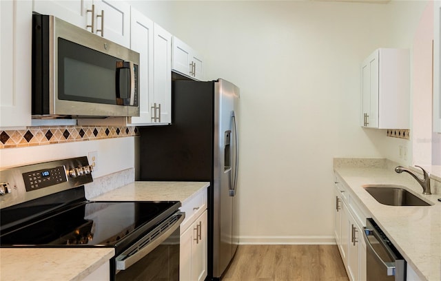 kitchen featuring white cabinets, appliances with stainless steel finishes, light stone counters, light hardwood / wood-style floors, and sink