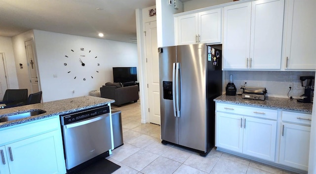 kitchen featuring light tile patterned floors, appliances with stainless steel finishes, stone countertops, white cabinetry, and sink