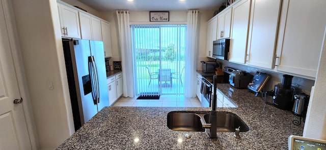 kitchen with dark stone countertops, white cabinetry, backsplash, light tile patterned floors, and appliances with stainless steel finishes