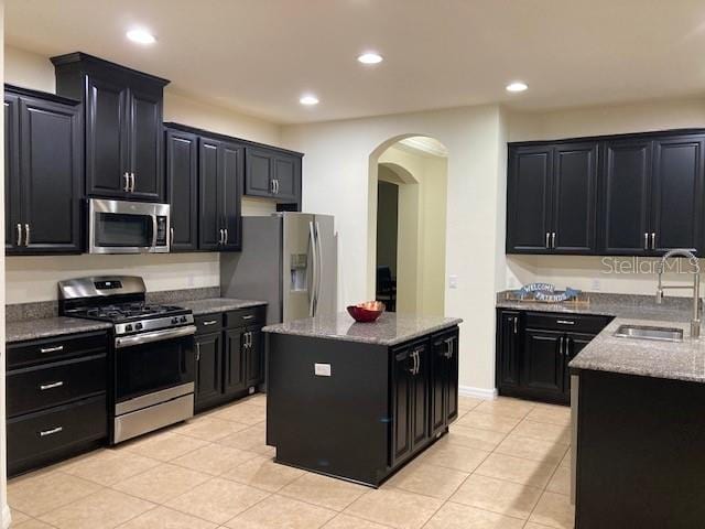 kitchen with light stone countertops, appliances with stainless steel finishes, a kitchen island, and sink