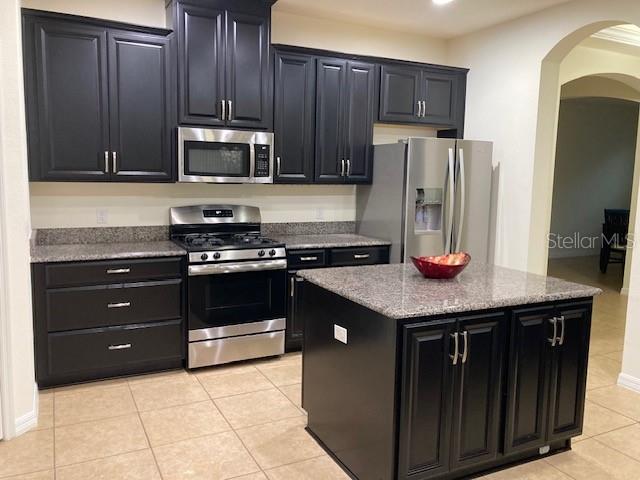 kitchen with appliances with stainless steel finishes, light tile patterned floors, a center island, and light stone counters