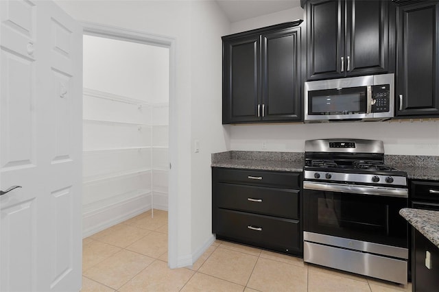 kitchen with light tile patterned floors, stainless steel appliances, and dark stone counters