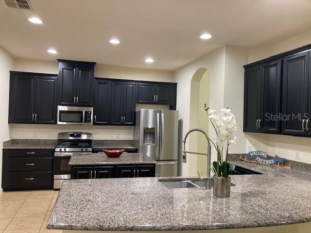 kitchen featuring appliances with stainless steel finishes, a kitchen island with sink, sink, stone countertops, and light tile patterned flooring