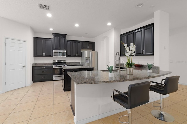 kitchen with appliances with stainless steel finishes, dark stone countertops, a breakfast bar area, and sink