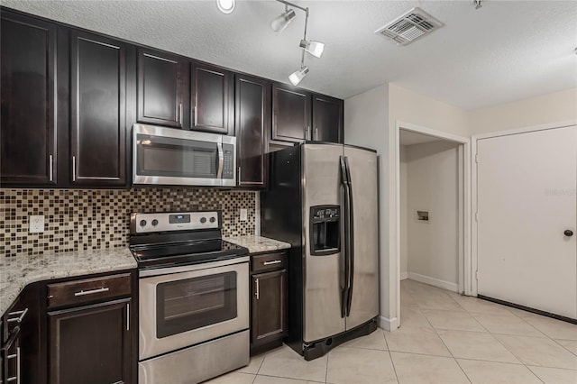 kitchen with backsplash, light stone counters, appliances with stainless steel finishes, and dark brown cabinets