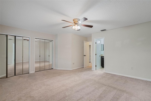 unfurnished bedroom with multiple closets, light carpet, ceiling fan, connected bathroom, and a textured ceiling