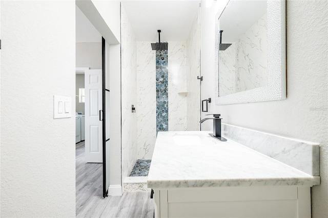 bathroom with tiled shower, vanity, wood-type flooring, and washer / clothes dryer