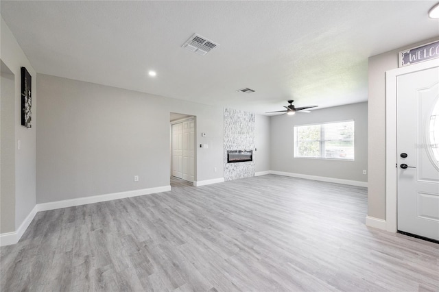 unfurnished living room featuring a fireplace, a textured ceiling, ceiling fan, and light hardwood / wood-style floors