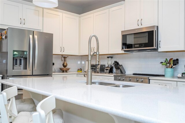 kitchen featuring stainless steel appliances, sink, white cabinets, a breakfast bar area, and decorative backsplash