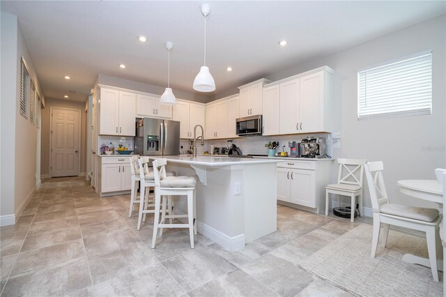 kitchen with white cabinets, stainless steel appliances, decorative light fixtures, and a kitchen island with sink