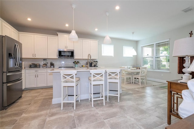 kitchen with stainless steel appliances, an island with sink, hanging light fixtures, a breakfast bar, and white cabinets