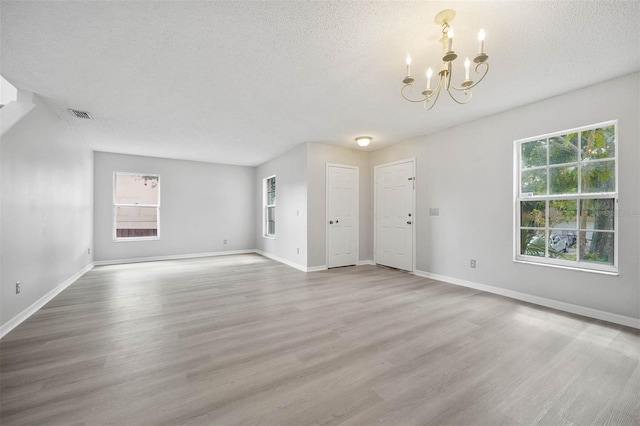 unfurnished living room featuring a textured ceiling, light hardwood / wood-style flooring, and an inviting chandelier