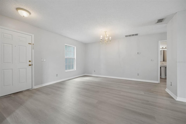 unfurnished room with a textured ceiling, an inviting chandelier, and light hardwood / wood-style floors