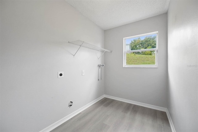 clothes washing area with a textured ceiling, hookup for an electric dryer, and light hardwood / wood-style floors