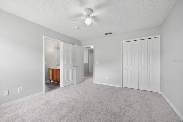 unfurnished bedroom featuring a textured ceiling, ensuite bath, ceiling fan, carpet, and a closet