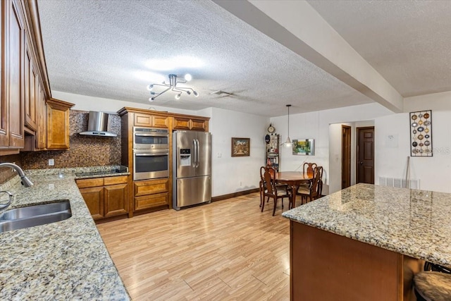 kitchen with light wood-type flooring, stainless steel appliances, sink, wall chimney range hood, and a textured ceiling