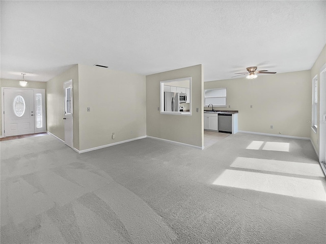 unfurnished living room with baseboards, visible vents, a sink, a textured ceiling, and light carpet