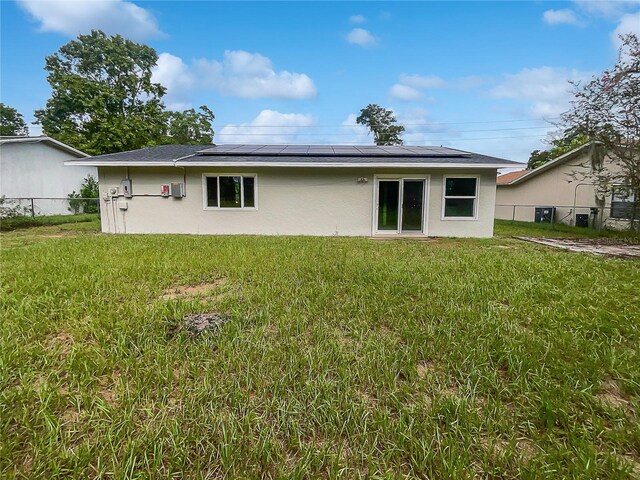 back of property featuring a yard and solar panels