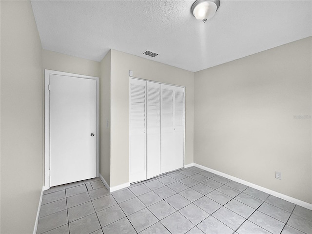 unfurnished bedroom featuring a textured ceiling, light tile patterned flooring, and a closet