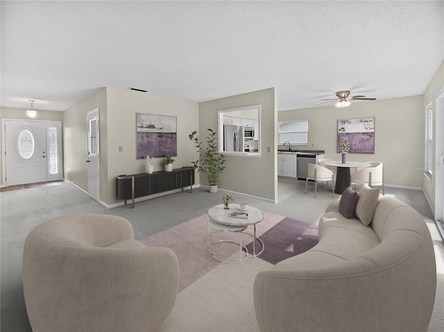 living room with visible vents, baseboards, ceiling fan, light colored carpet, and a textured ceiling