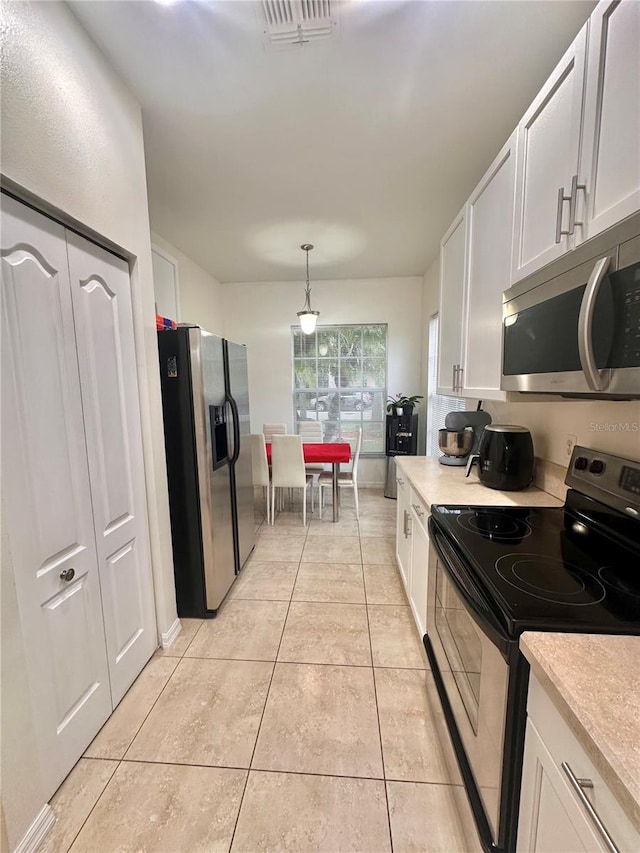 kitchen with white cabinets, appliances with stainless steel finishes, light tile patterned floors, and hanging light fixtures