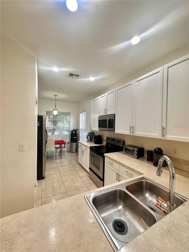 kitchen with white cabinets, light tile patterned floors, stainless steel appliances, sink, and pendant lighting