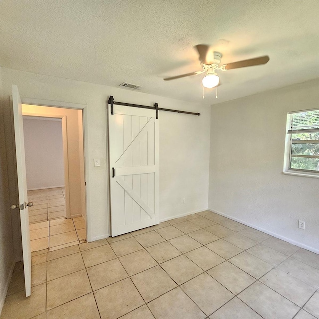 unfurnished bedroom featuring a textured ceiling, a barn door, ceiling fan, and light tile patterned flooring