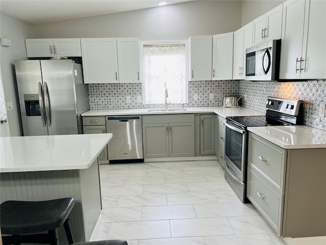 kitchen with backsplash, appliances with stainless steel finishes, a breakfast bar, sink, and lofted ceiling