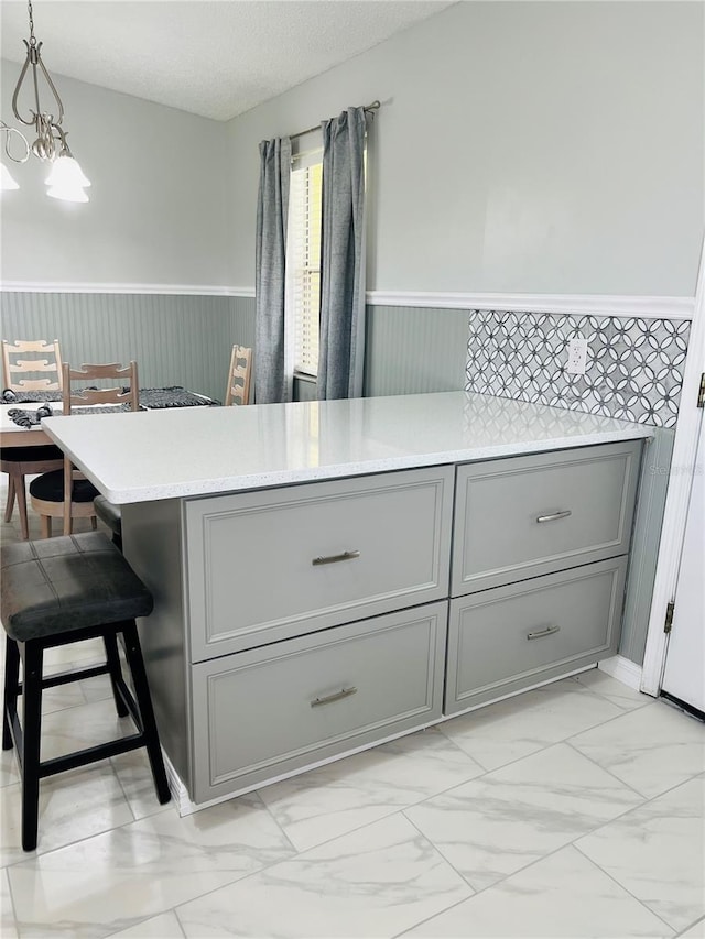 kitchen featuring gray cabinetry, decorative light fixtures, kitchen peninsula, a kitchen breakfast bar, and a textured ceiling