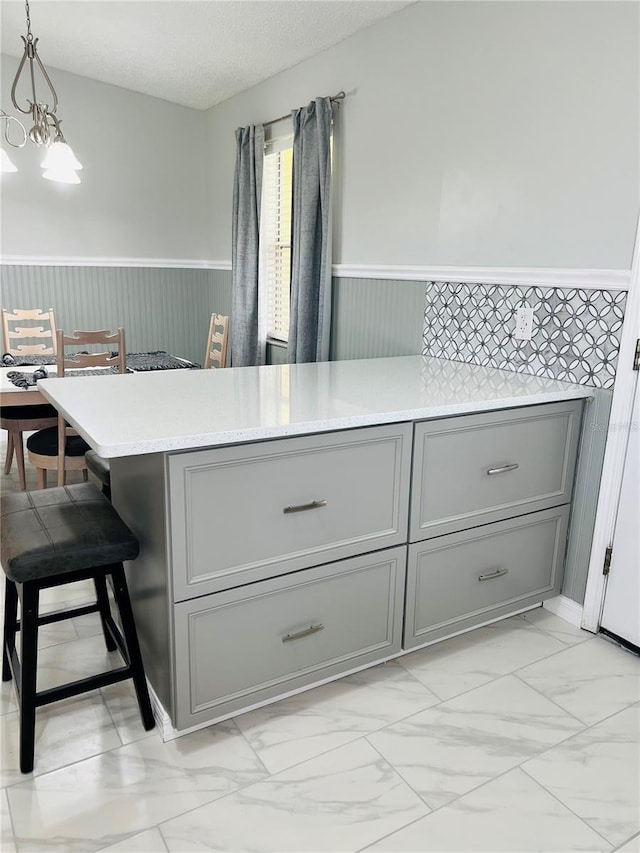 kitchen featuring a wainscoted wall, a breakfast bar area, marble finish floor, and gray cabinetry