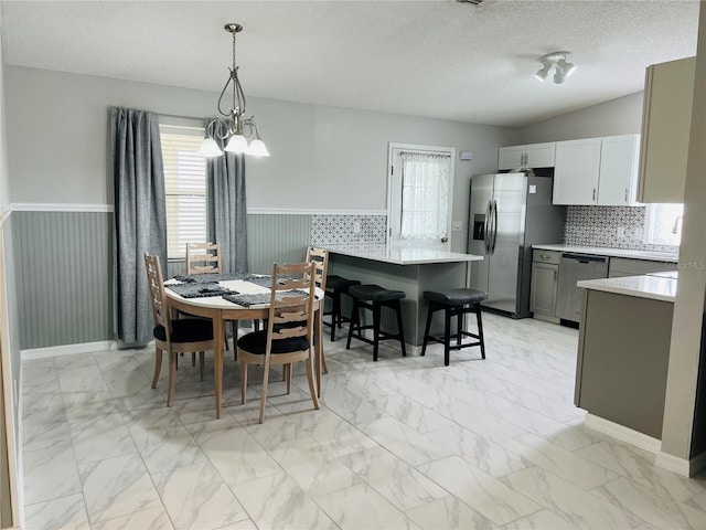 dining space featuring a wainscoted wall, wood walls, an inviting chandelier, marble finish floor, and a textured ceiling