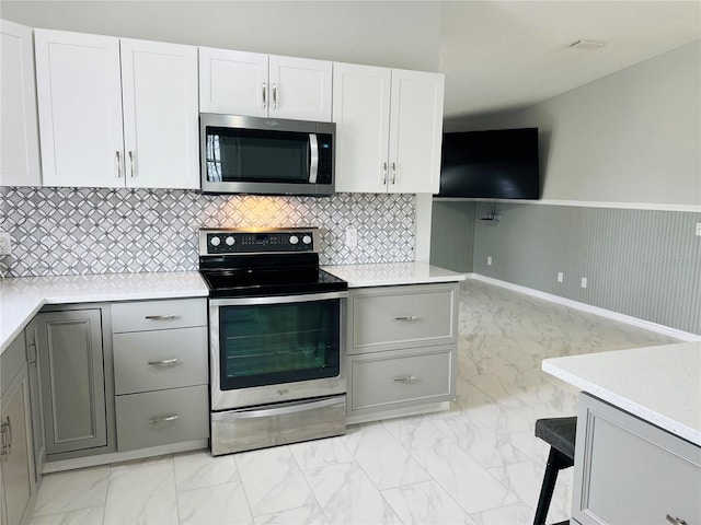 kitchen with stainless steel appliances, marble finish floor, a wainscoted wall, and gray cabinets