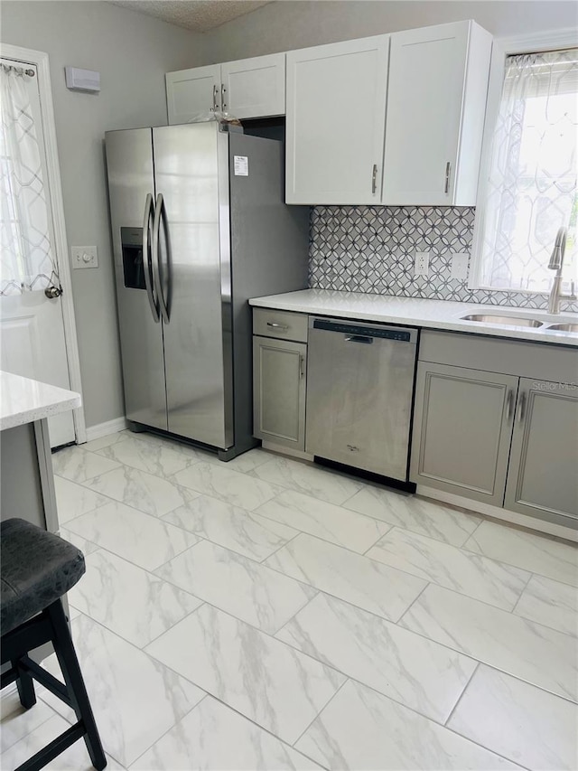 kitchen with a sink, marble finish floor, appliances with stainless steel finishes, and gray cabinetry