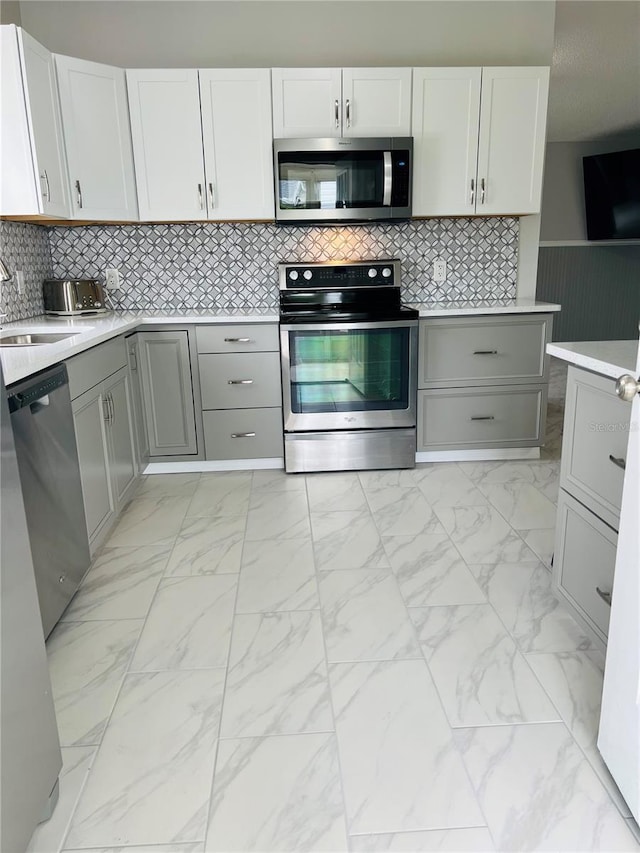 kitchen featuring a sink, gray cabinetry, light countertops, stainless steel appliances, and marble finish floor